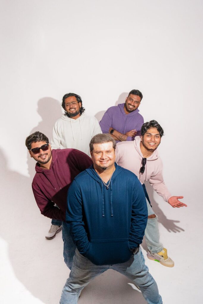 Five friends posing casually in a studio setting wearing colorful hoodies.